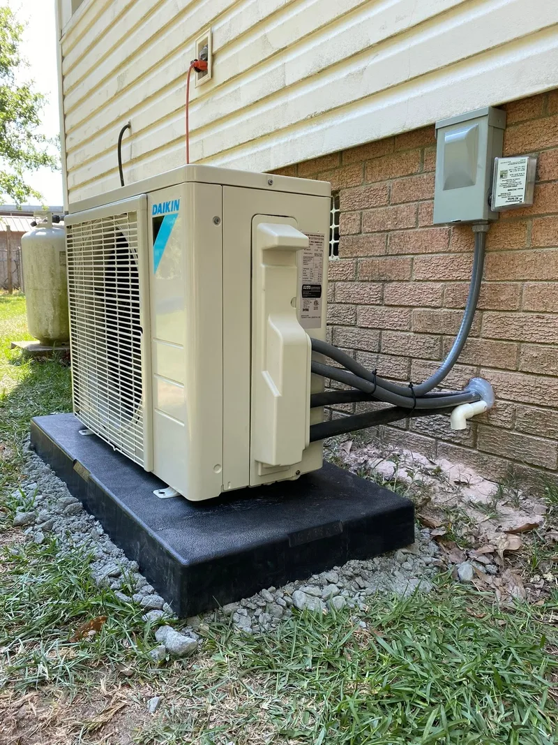 Daikin ductless outdoor unit installed on an equipment pad beside a home with brick and light siding.