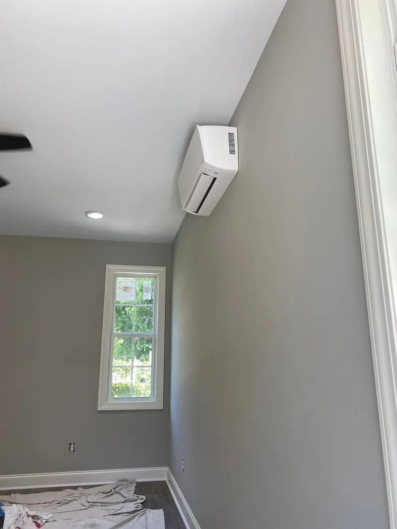 White wall-mounted ductless mini-split installed near the ceiling of a room with gray walls.