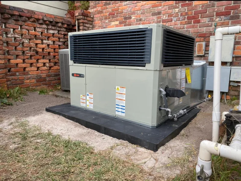 New Trane packaged HVAC unit on a black equipment pad with connected ductwork at the same brick enclosure.